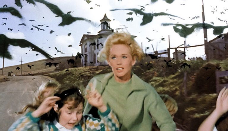 A still from the film The Birds showing Tippi Hedren and two children running from a flock of black birds